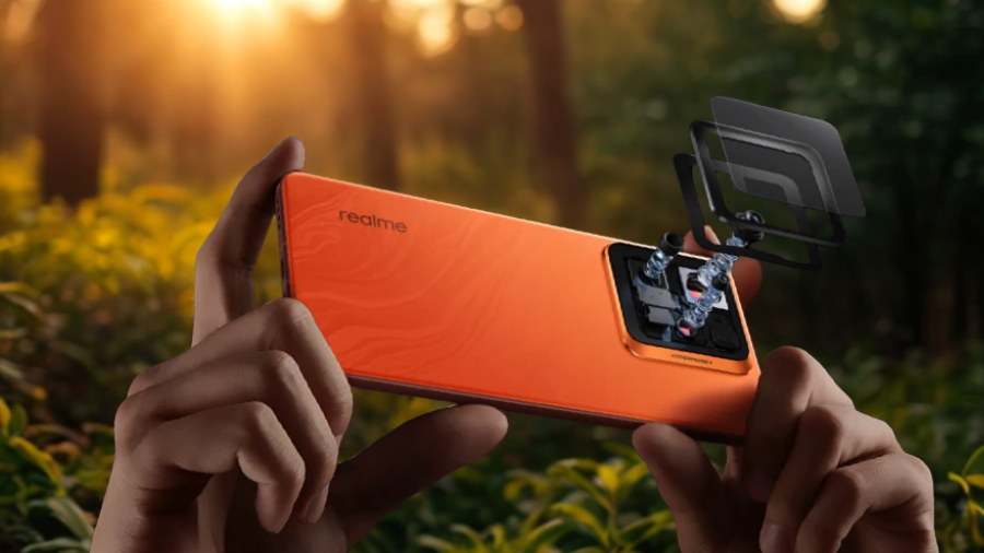 Ruce drží oranžový telefon Realme GT 7 Pro 5G s rozloženým modulem fotoaparátu, ukazující vnitřní komponenty a čočky, v pozadí les při západu slunce.