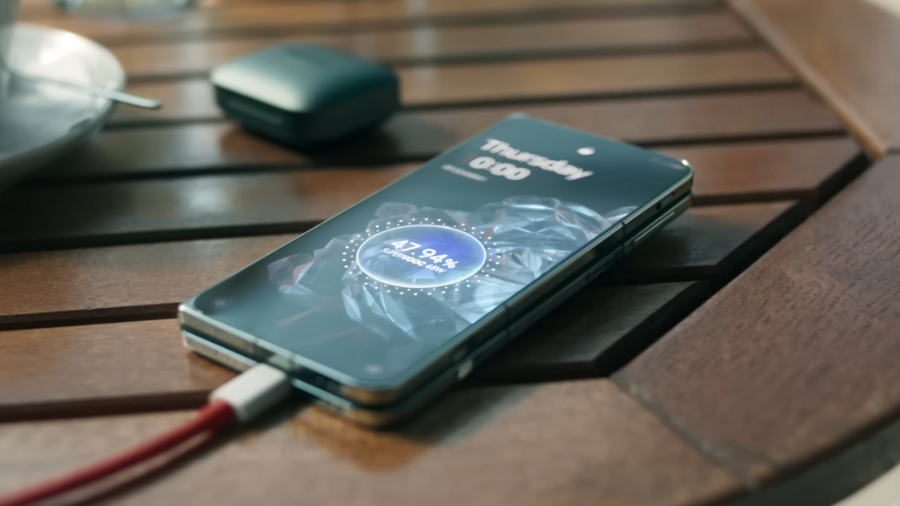 Složený telefon OnePlus Open ležící na dřevěném stole a nabíjející se pomocí kabelu. Na displeji se zobrazuje logo SuperVOOC a ukazatel nabíjení 47.94%.