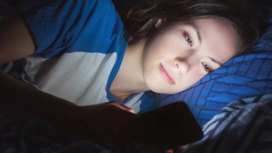 Osoba v noci ležící v posteli a dívající se na telefon Honor 200.