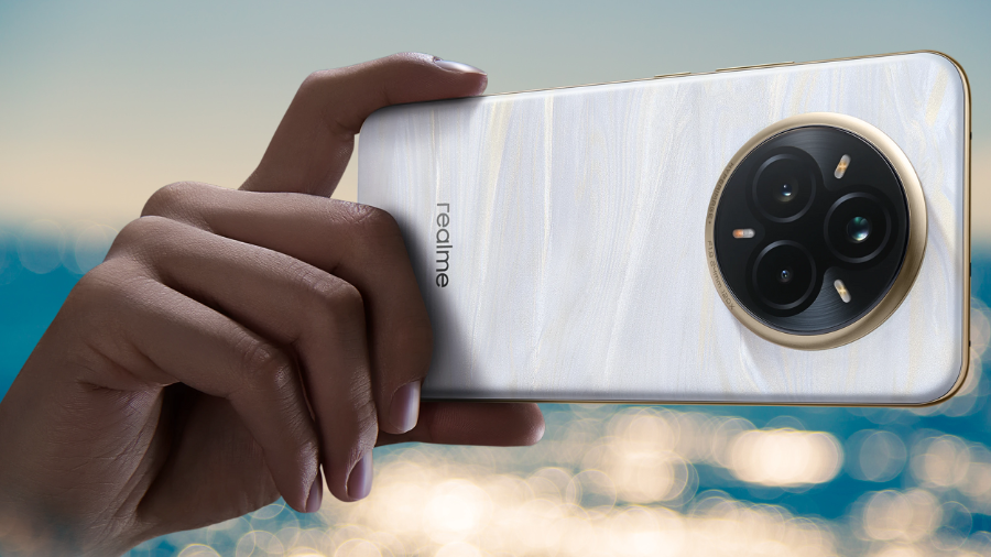 Ruka držící telefon Realme 14 Pro+ v perleťově bílé barvě s výhledem na moře, zaměřeno na zadní fotoaparát.