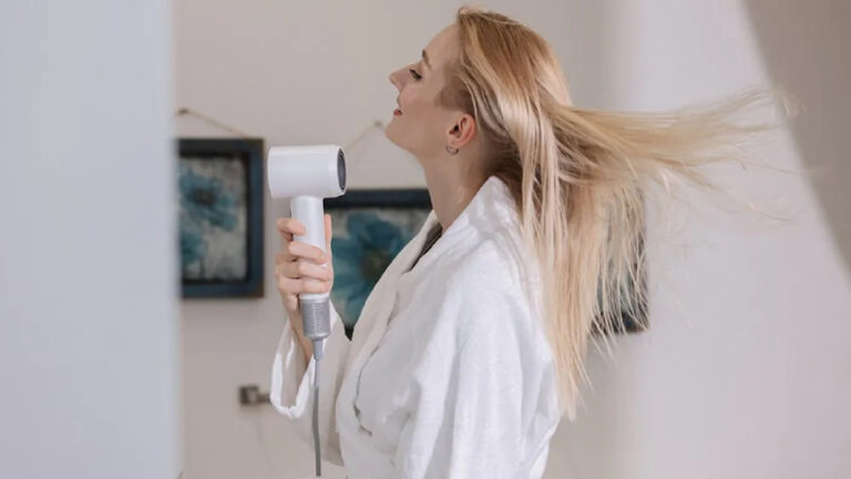 Fotografie ženy z profilu s dlouhými blond vlasy fénující si vlasy fénem Laifen Swift Special.