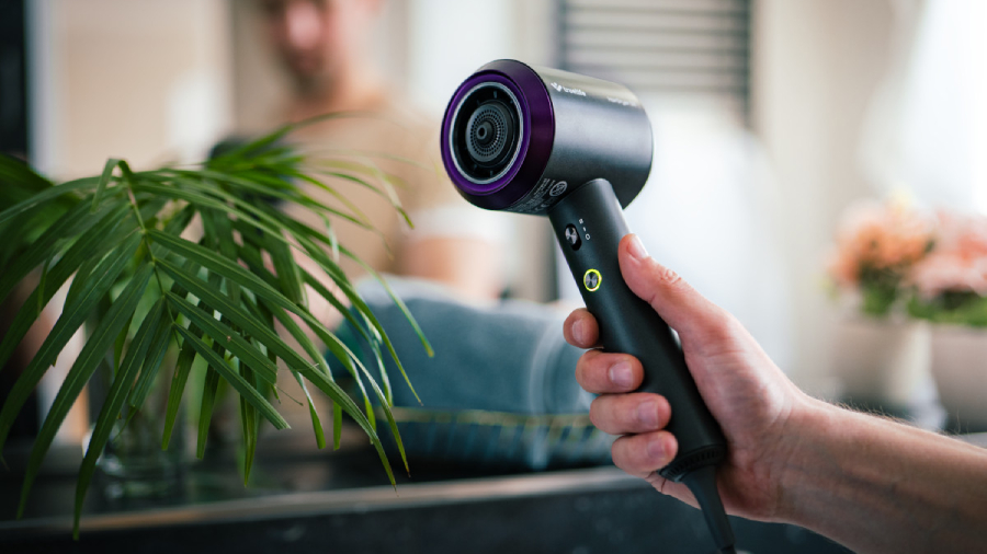 Fén TrueLife HairDryer D3 v ruce osoby v koupelně, ve které jsou pokojové květiny.