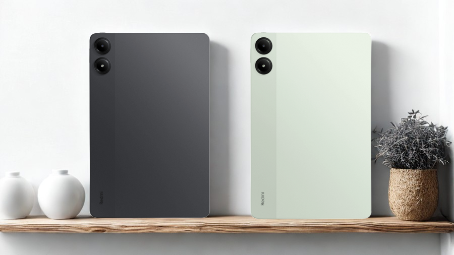 Dva tablety Xiaomi Redmi Pad Pro 5G, jeden v tmavě šedé a druhý ve světle zelené barvě, opřené o stěnu na dřevěné poličce.