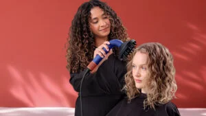 Kadeřnice fénuje vlasy ženě fénem Dyson Supersonic r s nasazeným difuzérem. Nejlepší fény roku.