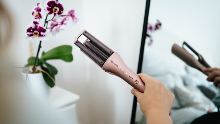 Na obrázku drží žena v ruce kulmu TrueLife HairWaver W6 pro naše srovnání kulem na vlasy.
