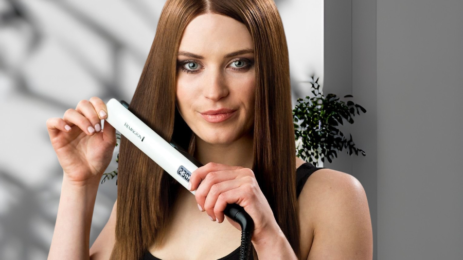 Usmívající se žena s dlouhými hnědými vlasy žehlící si vlasy žehličkou Remington S8500 Shine Therapy.