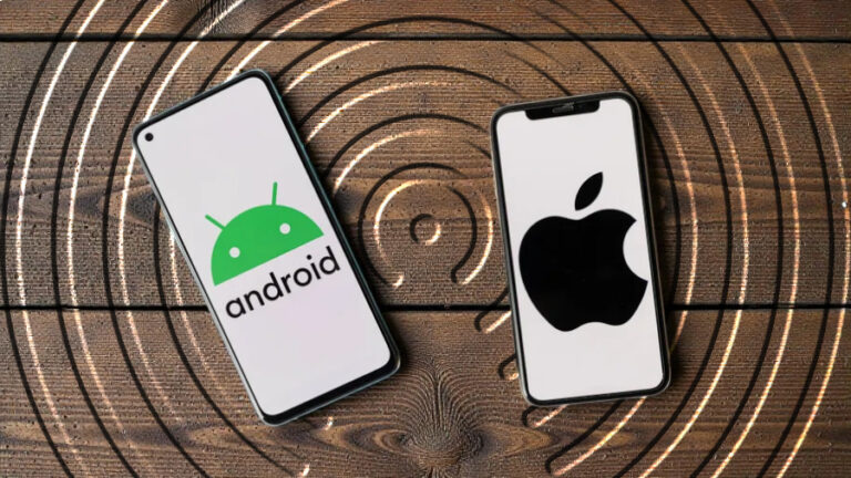 2 mobily vedle sebe, jeden má na displeji android a druhý znak Apple, oba telefony leží na dřevěném podkladu, na kterém je reliéf kruhového přenosu dat AirDrop.