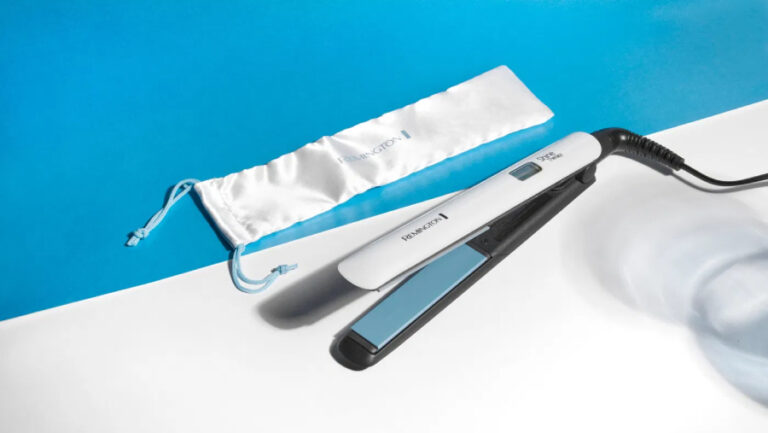 Žehlička na vlasy Remington S8500 Shine Therapy v bélém provedení položená na stole i se sáčkem.