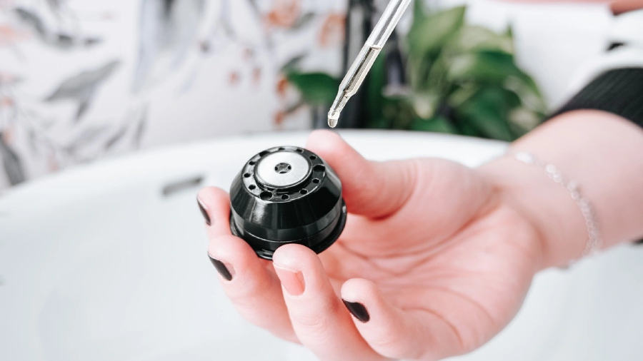 Detail ženské ruky, která kapátkem nalévá pečující olejíček do trysky pro nástavec Oil Therapy fénu Concept BLDC VV8100.