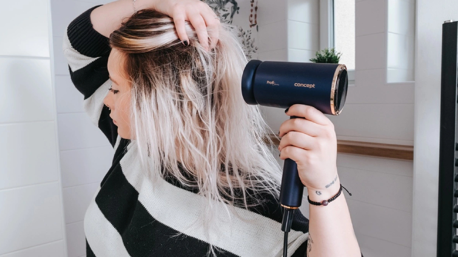 Žena v bíle obložené koupelně fénující si vlhké vlasy fénem Concept BLDC VV8100.