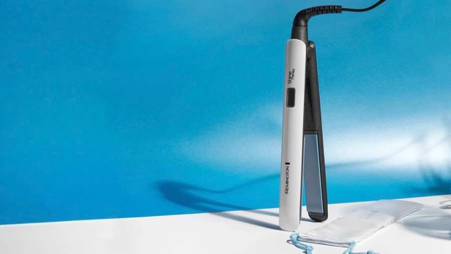 Žehlička na vlasy Remington S8500 Shine Therapy v bélí barvě postavená na bílém stole vedle níž leží bílý textilní cestovní obal.