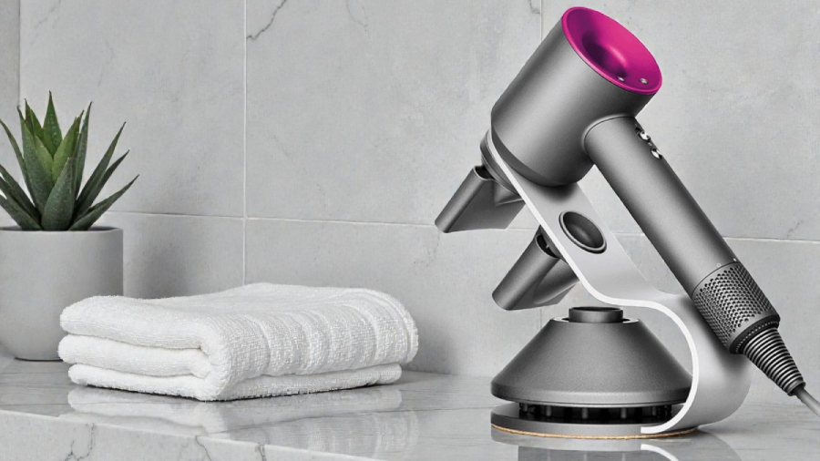 Fén Dyson Supersonic HD07 uchycený ve speciálním nástavci i s jeho nástavci, položený na mramorovém stole vedle ručníků v koupelně.