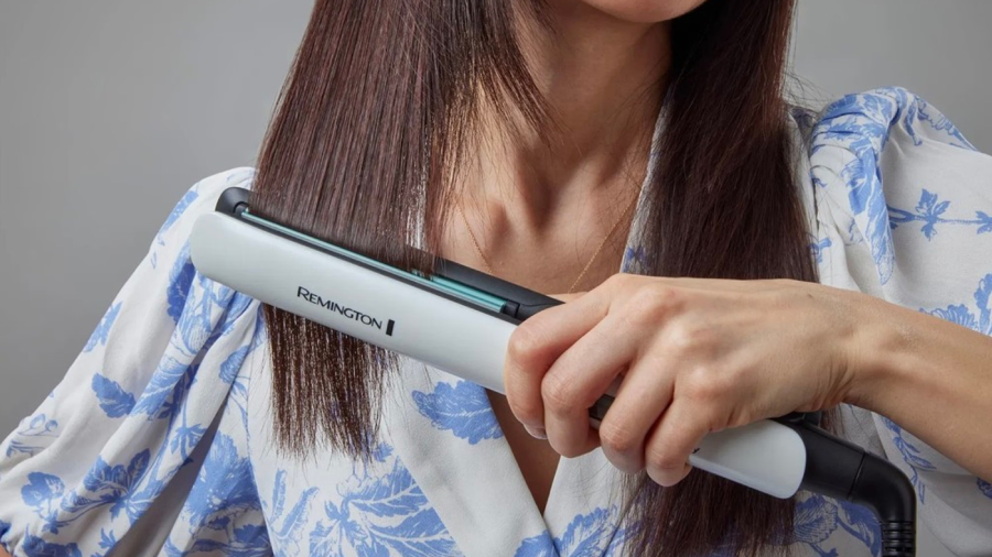 Detailní pohled na ruku ženy žehlící si pramen vlasů žehličkou Remington S8500 Shine Therapy.