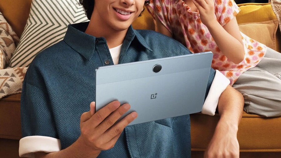 Muž drží tablet OnePlus Pad Lite s logem OnePlus uprostřed zadní strany, sedí na pohovce s dítětem.