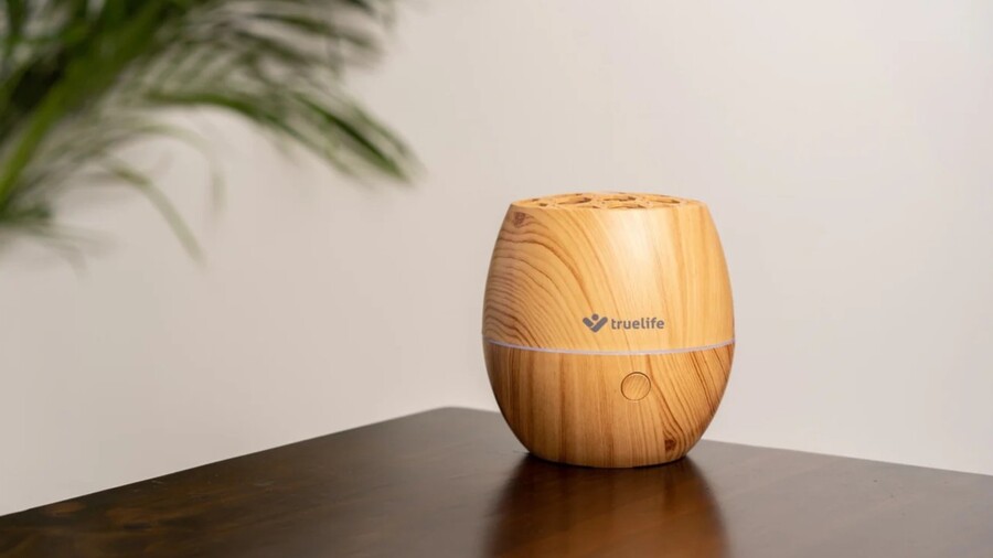 Tipy na vánoční dárky pro ženy: Detailní záběr na Aroma difuzér AIR Diffuser D3 Light s dekorem světlého dřeva, který stojí na tmavém lesklém stolku.