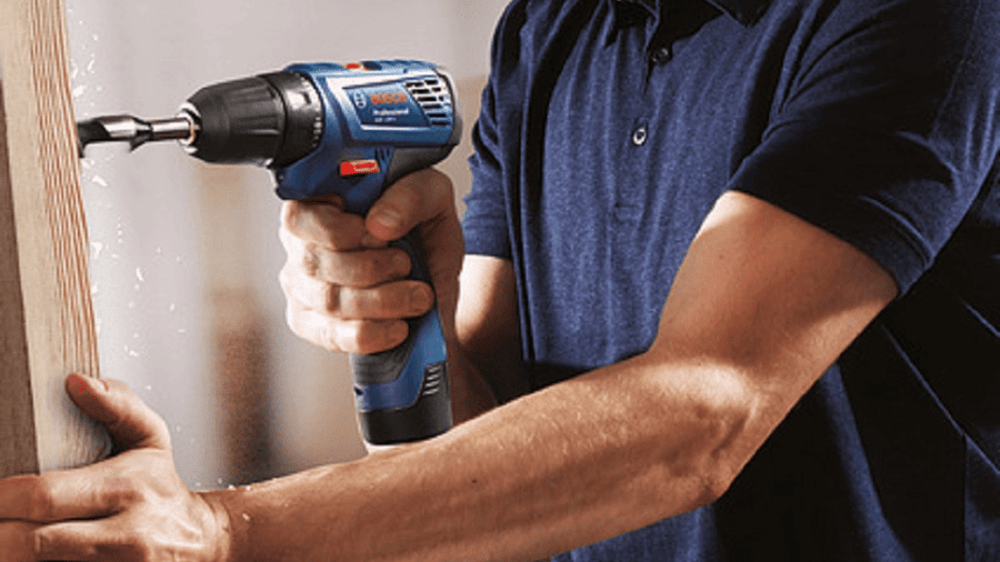 Muž drží v ruce vrtačku Bosch a vrtá do dřeva - nejlepší dárky pro muže.