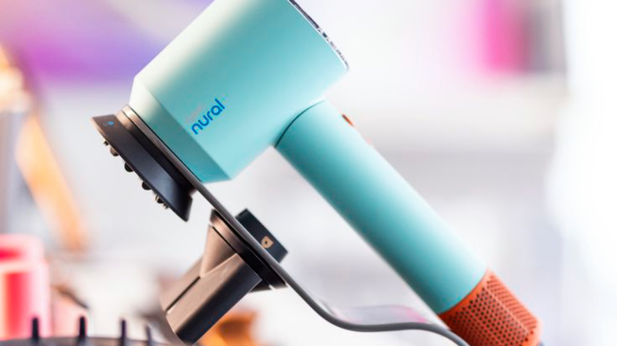 Fén Dyson Supersonic Nural v barvě Curly + Coily Ceramic patina/Topaz orange položený ve speciální stojanu. Pohled z boku.