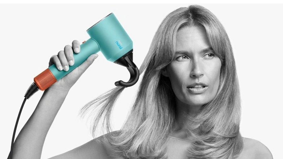 Žena na obrázku vyobrazená černobíle fénující si pramen vlasů fénem Dyson Supersonic Nural s nasazeným nástavcem proti polétavým vlasům, fén je na obrázku vyobrazen barevně, aby tak více vynikly jeho nádherné barvy.