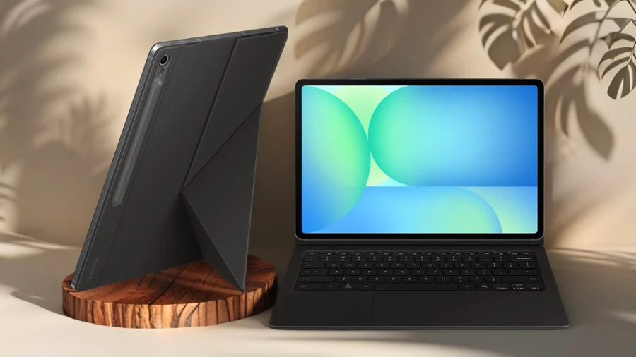 Samsung Galaxy Tab S10 FE s připevněnou klávesnicí Book Cover Keyboard leží otevřený na hnědém dřevěném podstavci, připomínající notebook. Druhý tablet je vedle něj v pouzdře, sloužícím jako stojan.