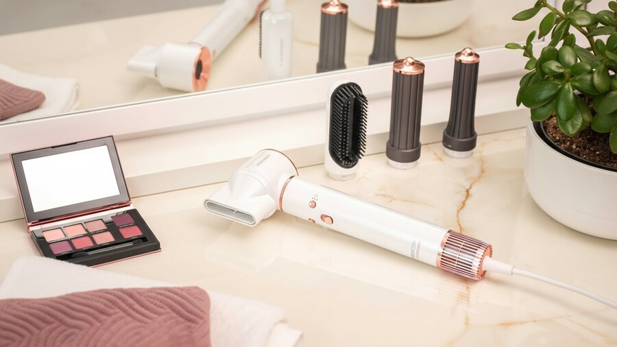 Tipy na vánoční dárky pro ženy: Kulmofén Sencor Artemiss SHS 9100RS s bílo-růžovými detaily leží na koupelnové desce s líčidly a vyměnitelnými kartáči.