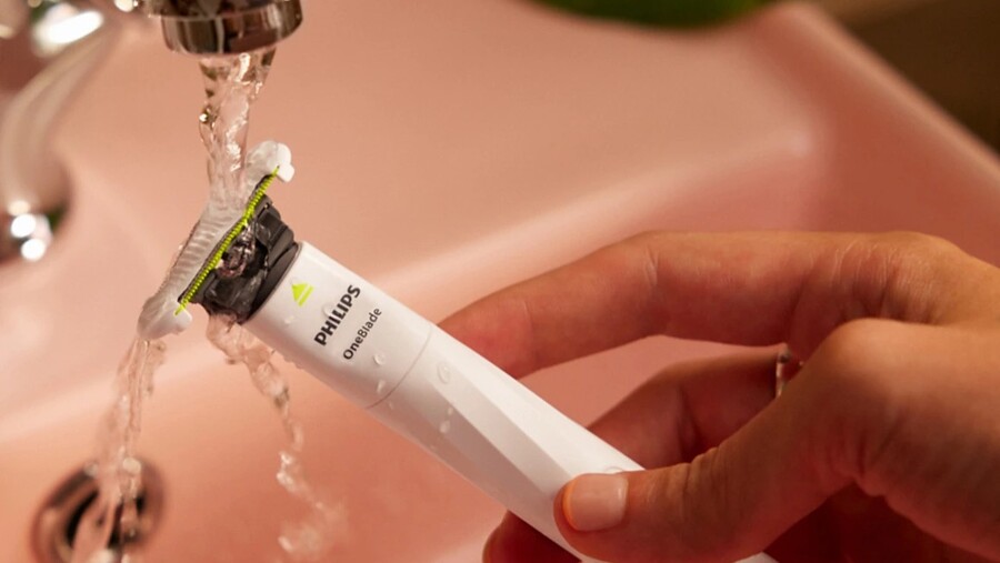 Tipy na vánoční dárky pro ženy: Holicí strojek Philips OneBlade Intimate QP1924/30 je držen pod tekoucí vodou v růžovém umyvadle, což demonstruje jeho voděodolnost.