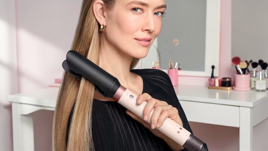 Žena s blond vlasy používá růžový kulmofén Dyson Airwrap Co-anda 2x™ s vyhlazujícím nástavcem pro dokonale rovný účes.