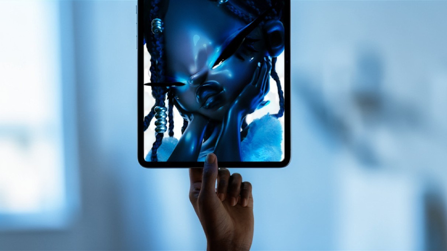 Ruka držící Apple iPad Pro 13" M5 s jasným Ultra Retina XDR displejem, na kterém je zobrazena detailní modrá 3D umělecká grafika postavy v profesionálním studiovém osvětlení.