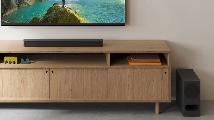 Černý soundbar Sony Bravia Theatre Bar 5 a bezdrátový subwoofer na minimalistickém dřevěném stolku pod televizorem.