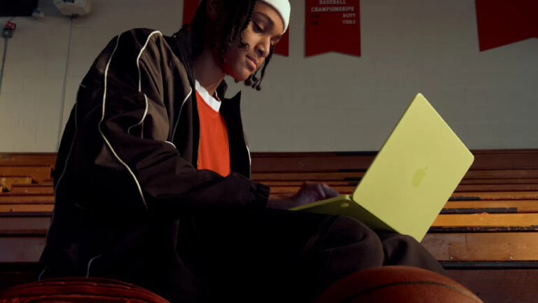 Student využívá výkonný MacBook Neo v barvě Citrus přímo v prostředí sportovní haly na tribuně.