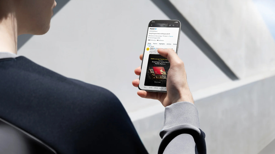 Pohled přes rameno muže držící smartphone POCO F8 Ultra, která v rukou se zájmem prochází příspěvek o procesoru Snapdragon 8 Elite na sociálních sítích venku v jasném slunném počasí.