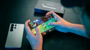 Update Samsungu. Muž drží telefon Samsung a hraje hry. Na stel druhý telefon a krabička