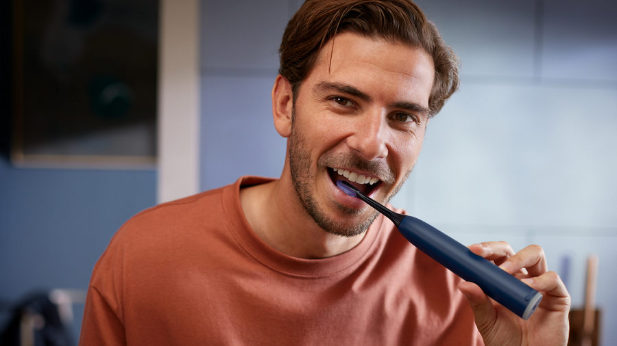 Muž si čistí zuby kartáčkem Philips Sonicare 7100 v tmavě modré barvě