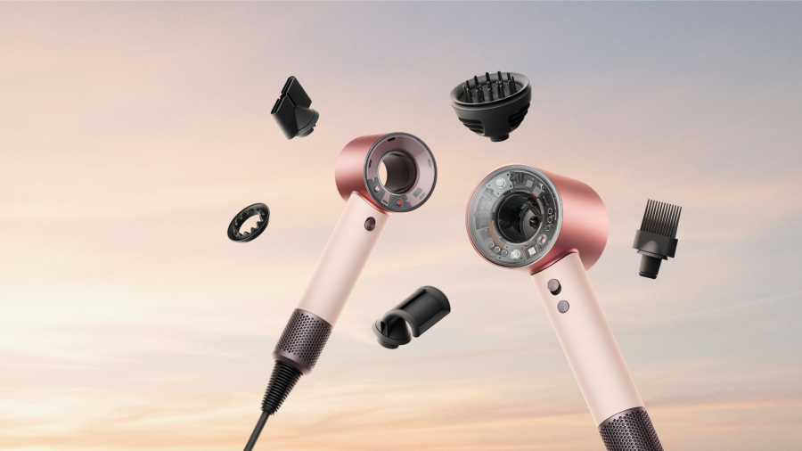 Dva fény Dyson Supersonic a Dyson Supersonic Travel v růžovo-zlatém provedení obklopené levitujícími magnetickými nástavci pro profesionální styling na pozadí západu slunce.