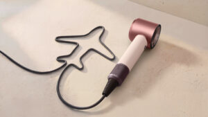 Cestovní fén Dyson Supersonic Travel s napájecím kabelem vytvarovaným do tvaru letadla na světlém minimalistickém pozadí.