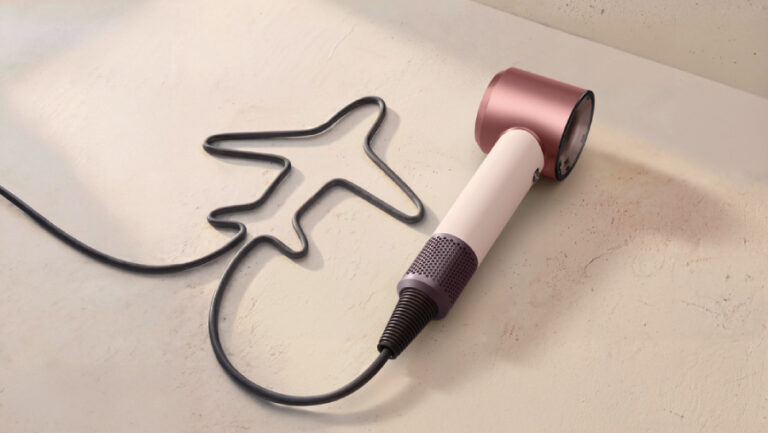 Cestovní fén Dyson Supersonic Travel s napájecím kabelem vytvarovaným do tvaru letadla na světlém minimalistickém pozadí.