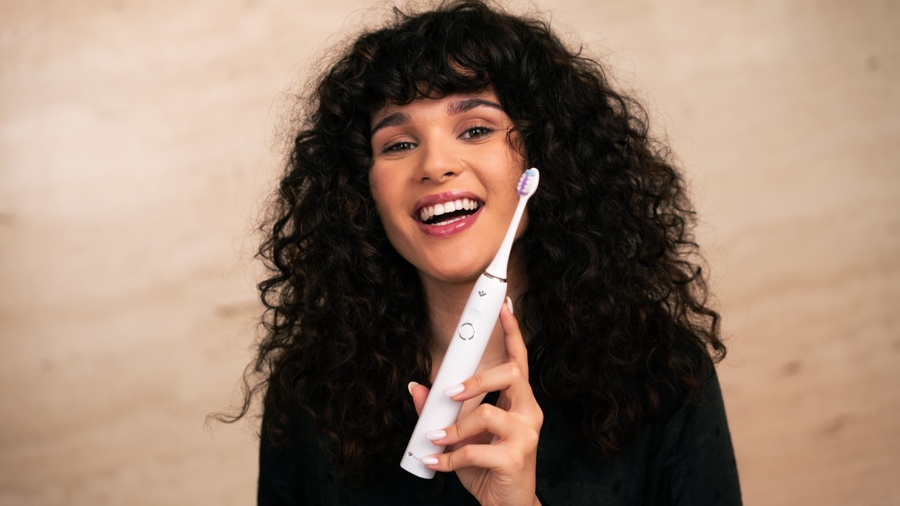 Žena je v koupelně a čistí si zuby u zrcadla kartáčkem TrueLife SonicBrush Clean70 UV