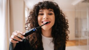 Žena je v koupelně a čistí si zuby u zrcadla kartáčkem TrueLife SonicBrush Clean70 UV