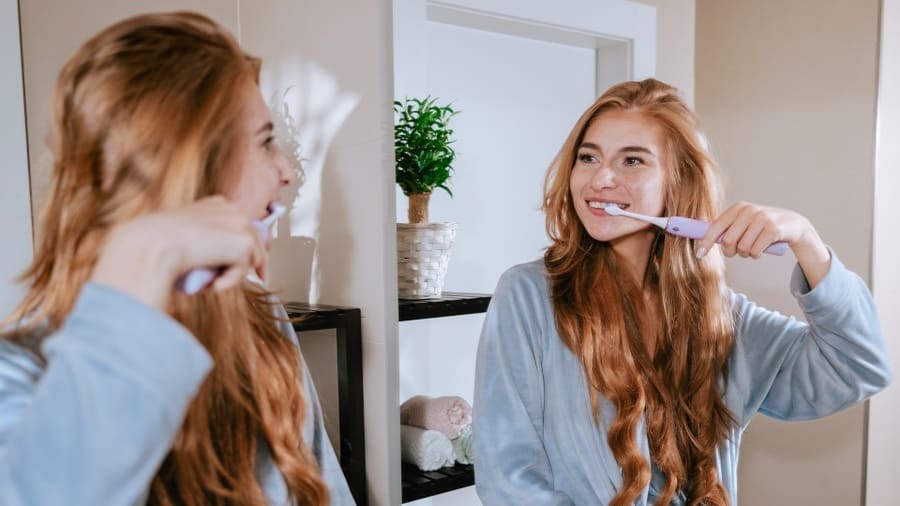 Žena si čistí zuby kartáčkem TrueLife SonicBrush Clean70 UV před zrcadlem