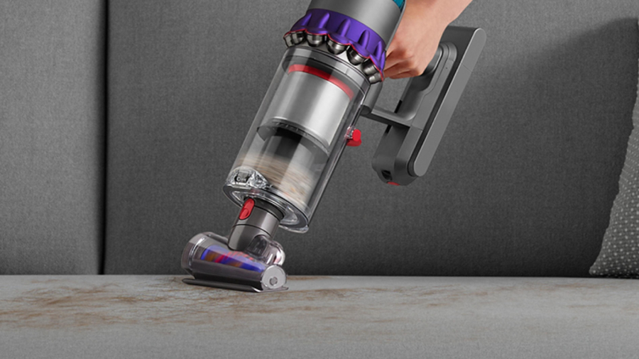 Detailní záběr na vysavač Dyson Gen5detect Absolute s kónickou hubicí, která efektivně odstraňuje prach a zvířecí chlupy z povrchu šedé pohovky.