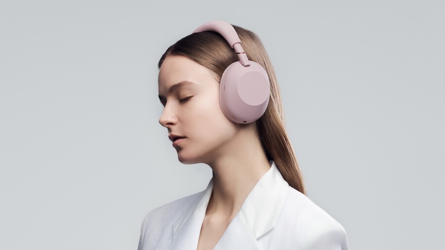 Boční profil ženy v bílém saku se sluchátky Sony WH-1000XM6 v barvě Sand Pink.
