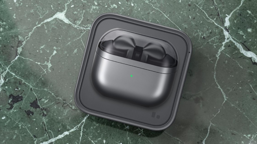 Stříbrné nabíjecí pouzdro se sluchátky Samsung Galaxy Buds3 Pro s průhledným víkem a svítící zelenou LED kontrolkou nabíjející se na bezdrátové stanici, umístěné na mramorované zelené podložce.