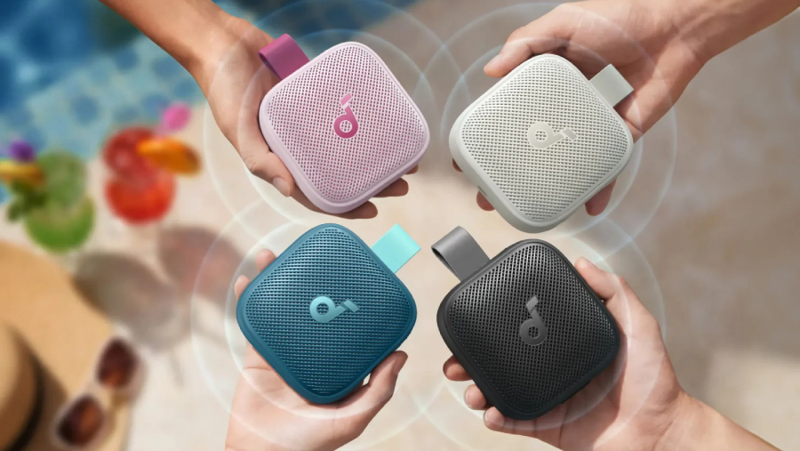 Čtyři přenosné reproduktory soundcore Boom Go 3i v růžové, béžové, modré a černé barvě držené v rukou nad stolem a bazénem.