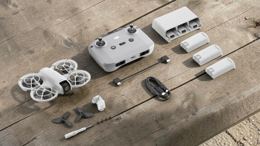 Rozložený obsah balení DJI Neo Fly More Combo s dronem, dálkovým ovladačem, třemi bateriemi, nabíjecím hubem a náhradními díly na dřevěném stole.
