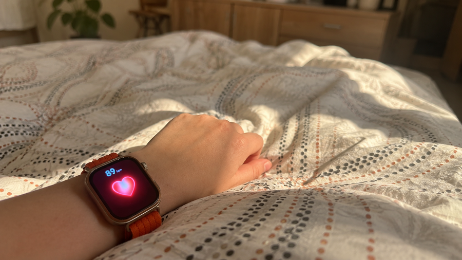 Detailní pohled na Huawei Watch Fit 5 Pro na zápěstí v posteli, zobrazující měření srdečního tepu (89 bpm) s ikonou srdce.