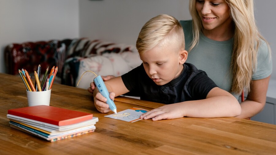 Inspirace na dárky ke Dni dětí 2026: Chlapec kreslí 3D perem LAMAX ArtKid 3D žlutý obrázek, maminka ho při tvoření sleduje.