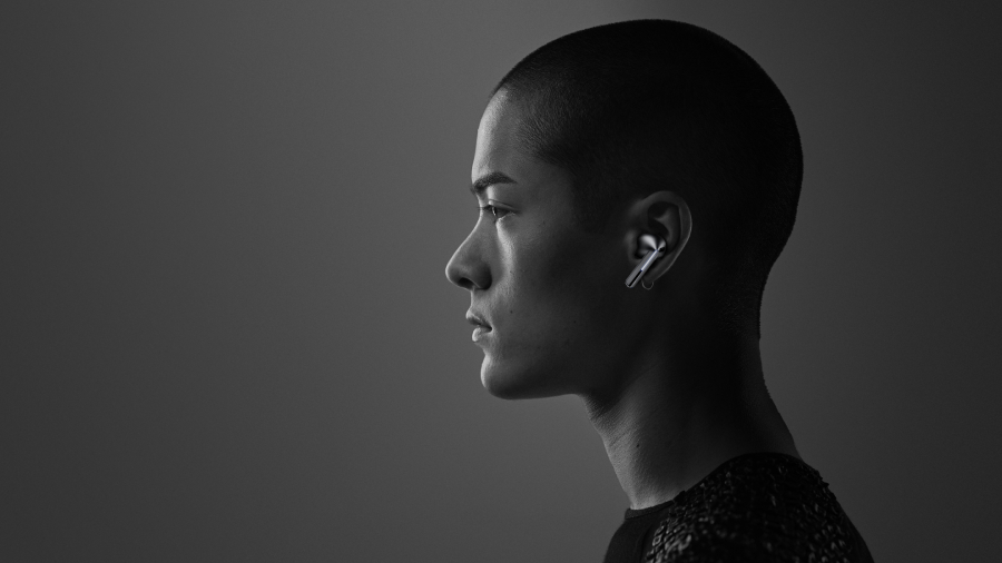 Boční profil osoby se stříbrným bezdrátovým sluchátkem Samsung Galaxy Buds3 Pro v uchu na tmavém pozadí.
