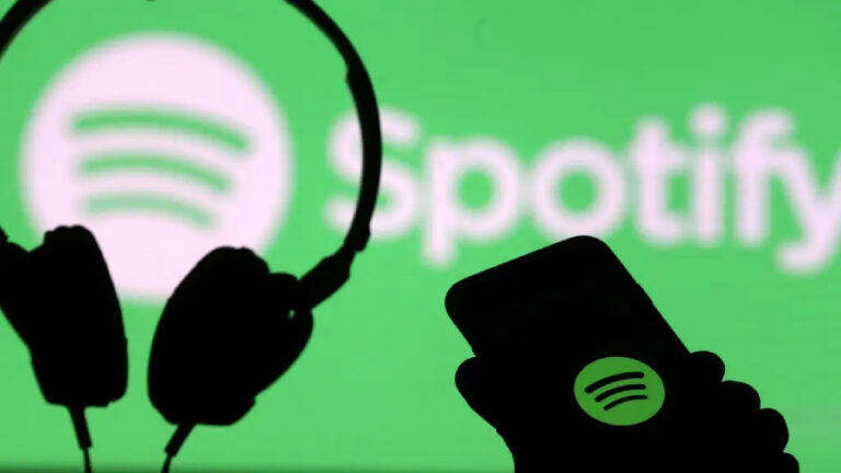 Silueta ruky držící chytrý telefon s logem Spotify a silueta sluchátek položených před velkou zelenou obrazovkou, na které je bílé logo a nápis Spotify.