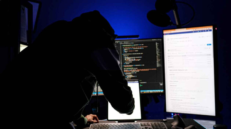 Silueta hackera v mikině s kapucí v temné místnosti plné monitorů s kódem, kde umělá inteligence ohrožuje bezpečnost.
