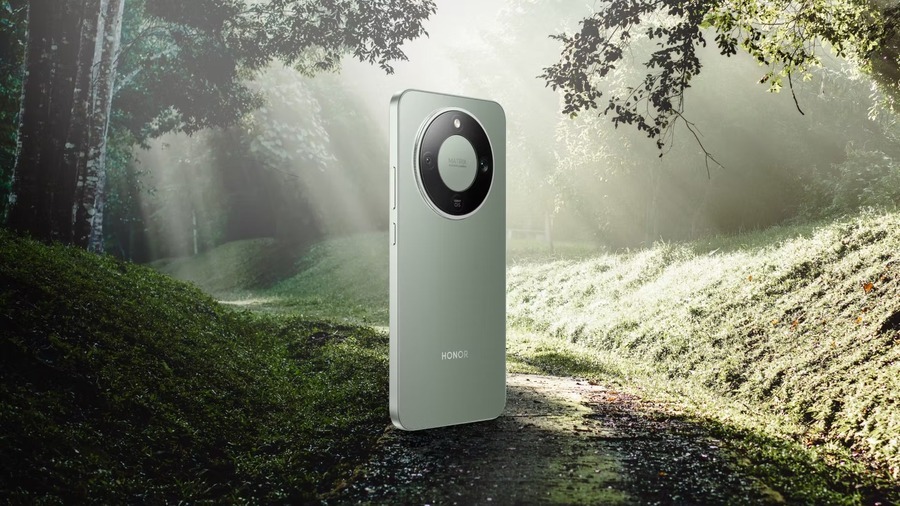 Mobilní telefon Honor Magic8 Lite v zeleném provedení zasazený do lesního prostředí. Pohled na zadní stranu s kruhovým fotomodulem na pozadí lesní cesty zalité slunečními paprsky.