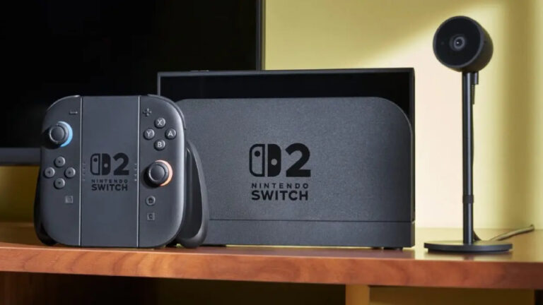 Herní konzole Nintendo Switch 2 v černé dokovací stanici vedle Joy-Con ovladačů a externí kamery na dřevěném TV stole.